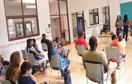 a lecture given to a classroom full of people, some with infants on their laps